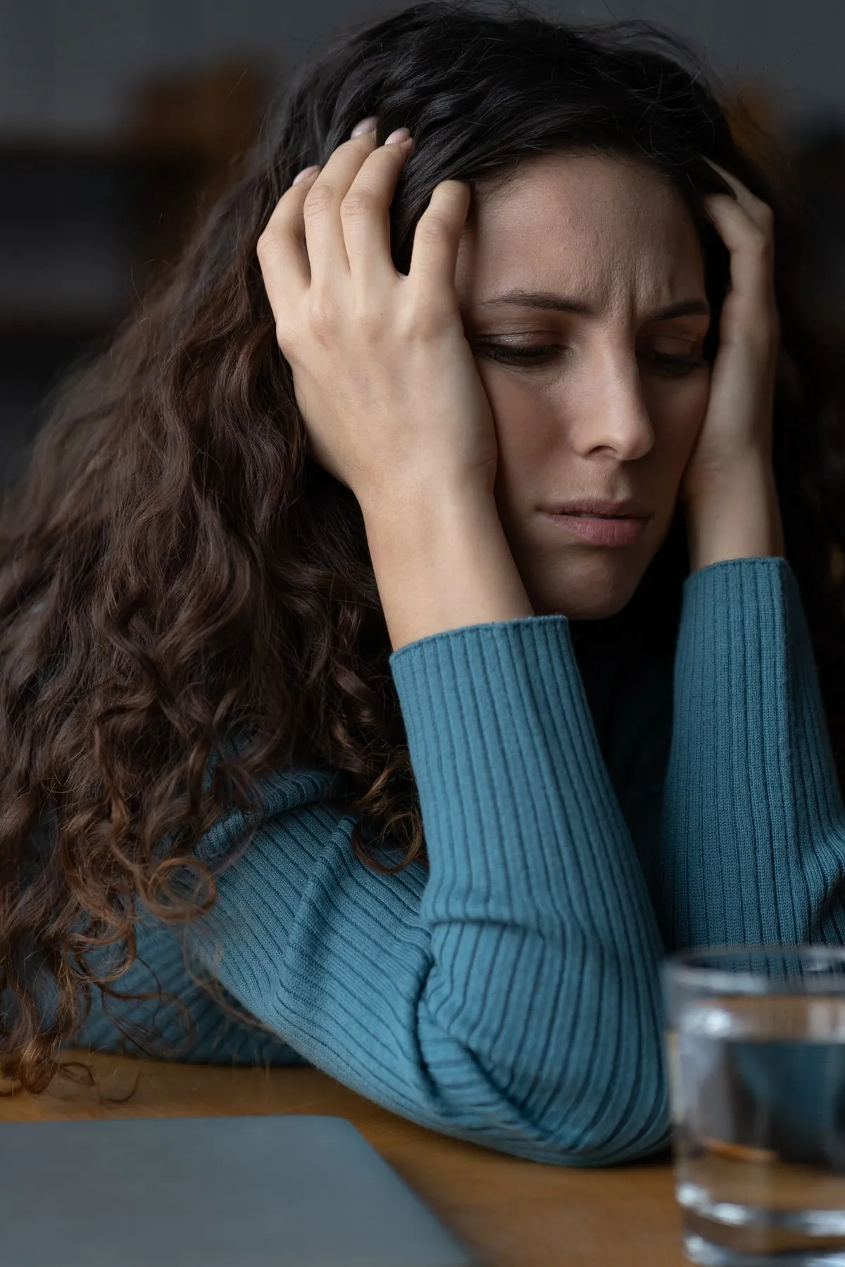 Woman with curly hair resting her head in her hands, looking distressed