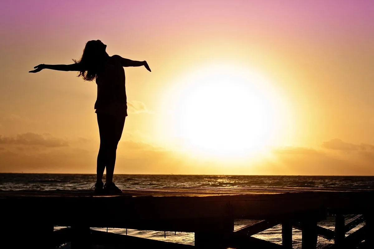 Silhouette of a woman with arms outstretched against a sunset over the sea